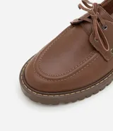 Zapato estilo dockside de cuero color marrón, con puntera redonda, cordones frontales y suela track dentada.