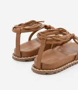 Sandalia plana color marrón con tiras finas que se atan al tobillo y suela con pespuntes en contraste.