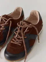Championes de cuero con diseño combinado en color marrón y negro. Presentan una estructura de gamuza marrón con refuerzos de cuero liso negro en la puntera y laterales, cordones bicolores y suela de goma.