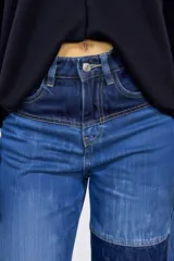 Pantalón de jean de corte recto y tiro alto, con diseño patchwork que combina diferentes tonos de denim azul y negro. Presenta bolsillos delanteros funcionales y cierre frontal con botón.