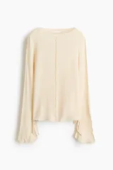 Top de punto fino y liviano color beige, con escote bote, mangas largas acampanadas con tiras decorativas en los puños y costuras visibles en la parte frontal y las mangas.