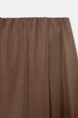 Pantalón marrón de tiro bajo con cintura elástica y corte muy holgado, estilo baggy o harén, con pliegues pronunciados en la parte delantera que crean un efecto asimétrico y drapeado en las caderas.