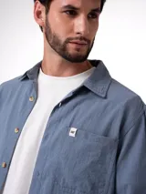 Camisa de manga larga con corte relajado, confeccionada en algodón con textura ligera. Presenta cierre frontal con botones, cuello clásico, puños abotonados y un bolsillo en el pecho con etiqueta de la marca Cat.
