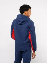 Campera deportiva Umbro del Club Nacional de Football, modelo Summit. Presenta un diseño con bloques de color en azul, rojo y blanco, con capucha, cierre frontal y bolsillos laterales con cierre. Incluye el logo de la marca y el escudo del club en el pecho.