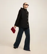 Saco corto negro de polivelour con capucha, cuello alto con cremallera, abotonado delantero cruzado, bolsillos delanteros y mangas largas.