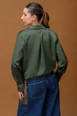 Camisa de seda color verde oliva, de corte holgado con cuello clásico, mangas largas con puños abotonados y cintura elástica que define la silueta.