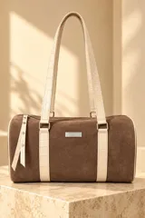 Cartera estilo baulito de cuero marrón tipo gamuza con detalles y tiras de hombro en cuero sintético texturizado color beige claro con patrón de cocodrilo. Cuenta con cierre superior y placa metálica frontal con el logo de la marca.