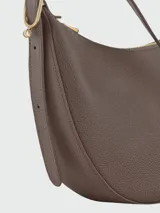 Cartera tipo bandolera de cuero granulado, con diseño de media luna y correa ajustable. Cuenta con cierre superior y herrajes metálicos discretos.