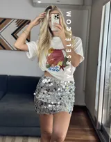 Remera blanca de cuello redondo y manga corta con estampado de paisaje costero en tonos naranja, rojo, verde y azul.