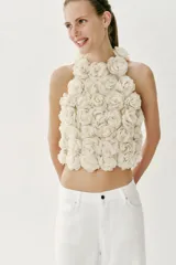 Top corto de cuello halter, confeccionado con una estructura de tejido que forma flores en relieve por toda la prenda. Presenta cierre en la espalda con abertura y botón oculto.