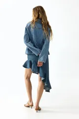 Pollera midi de denim de algodón rígido, con diseño asimétrico, tiro medio, pinzas en la cintura y volado con volumen en el borde inferior.