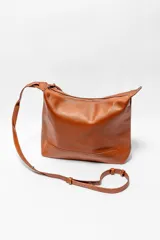 Bolso de hombro tipo hobo, confeccionado en cuero texturizado color marrón. Presenta un diseño minimalista con cierre superior, correa ajustable y detalle de tiras decorativas en el lateral.