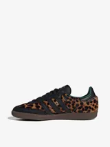 Championes Adidas Samba OG con estampado de guepardo, detalles en cuero negro, forro interior verde y suela marrón. Zapatilla de corte bajo con cordones negros y las tres tiras características de Adidas en cuero negro.