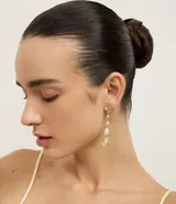 Aros colgantes dorados con diseño de hilo, decorados con perlas sintéticas en degradé y dijes en forma de concha marina.