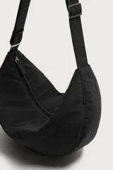 Bolso de hombro tipo hobo de nylon negro, con diseño curvo y asa ajustable. Cuenta con compartimento principal con cierre de cremallera y bolsillo interior con cremallera.