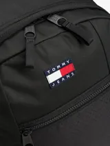 Mochila estilo retro de la marca Tommy Jeans, color negro, inspirada en modelos utilitarios. Cuenta con compartimento principal con cierre de cremallera, bolsillo exterior con cremallera, panel delantero con textura acolchada y parche con el logo de la marca en la parte superior. Incorpora correas ajustables, asa superior y detalles de tiras trenzadas.