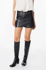 Mini falda de cuero negro con diseño cruzado en el frente y detalle de tachas metálicas circulares en la cintura.