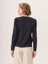 Remera blanca de manga larga con escote en V y detalles de alforzas verticales en el frente y mangas.