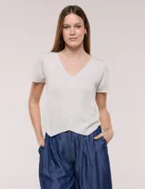 Cardigan corto de tejido de punto fino con hilo brillante de lurex y destellos metalizados. Presenta escote en V pronunciado, mangas cortas, cierre frontal con botones a tono y ruedo con terminación en pico en el frente.