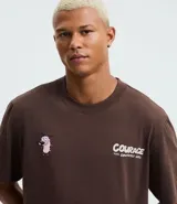 Remera masculina modelo comfort de algodón color marrón, con cuello redondo y mangas cortas. Presenta una estampa del personaje Coraje el Perro Cobarde en la espalda, con el texto "GOOD, GOOD DOG! COURAGE!".