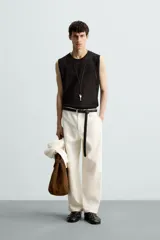 Chaleco de punto negro, con cuello redondo y manga sisa, confeccionado en tejido con estructura abierta (calado). Presenta bajo con aberturas laterales y acabados en rib.