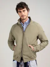 Campera Harrington color beige, con cuello alto abotonado, cierre frontal completo y bolsillos laterales con solapa y botones a presión. Puños y cintura elastizados de rib.