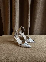 Zapato de tacón con punta fina, confeccionado en tela con aplicación de strass en la capellada y detalles en cuero en el talón, taco y pulsera. Cuenta con cierre de hebilla al tobillo y taco de altura media.