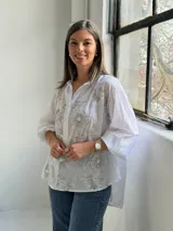 Camisa blanca de corte holgado y manga larga, con delicados bordados florales en tono gris claro en el frente.