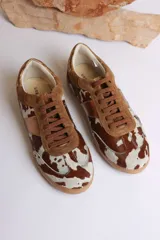 Zapatillas deportivas con estampado animal print de vaca en blanco y negro, con detalles en cuero sintético plateado en los laterales y talón.