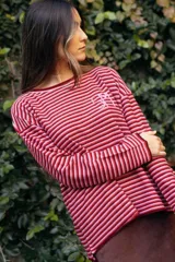 Remerón de manga larga y tejido de punto, con diseño de rayas finas horizontales en tonos rojos y rosados. Presenta cuello redondo y logo bordado a mano en el pecho.