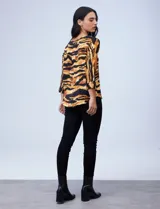 Blusa de gasa satén estampada con diseño animal print en tonos naranja y negro, de la marca Ninety. Tiene mangas tres cuartos y cuello redondo.