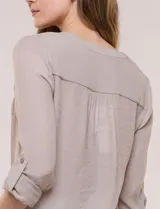 Blusa de calce relajado color salmón, confeccionada en tela liviana con textura sutil. Presenta escote en V con abotonadura frontal, bolsillo parche en el pecho, mangas largas regulables con presilla y ruedo con opción de anudar en el frente.