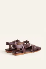 Sandalias planas tipo huarache de cuero negro, con tiras entrelazadas a mano y tira ajustable en el talón con hebilla metálica.