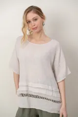 Blusa de lino color blanco, de corte amplio, con escote redondo, mangas cortas y detalle de guarda calada horizontal en la parte inferior.