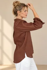Camisa de lino color blanca, con cuello clásico, mangas tres cuartos abullonadas en los hombros y terminación con volados en los puños, cierre frontal con botones ocultos.