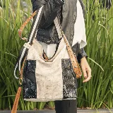 Bolso tipo hobo de cuero vacuno color beige con detalles en cuero negro con textura de reptil. Tiene cierre en la tapa trasera y bolsillos laterales. Incluye correa corta y dos correas extensibles y removibles para usar como morral.