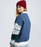 Suéter de punto jacquard de manga larga y cuello redondo con diseño invernal que incluye montañas, un teleférico rojo y un oso esquiando, con terminaciones caneladas en puños y ruedo.