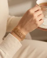 Set de cuatro brazaletes tipo esclava de acero con baño de oro, con textura martillada y detalle de circonias incrustadas.