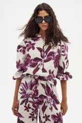 Camisa de lino con estampado floral grande en tonos morados sobre fondo blanco. Presenta cuello mao, manga corta abullonada con elástico en el puño y cierre frontal de botones.