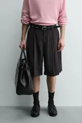 Bermuda negra de corte ancho (wide fit) confeccionada en tejido con mezcla de viscosa. Presenta pliegues en el delantero, bolsillos frontales y bolsillos de vivo en la parte trasera. Cierre frontal con cremallera y gancho metálico oculto.