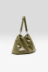 Bolso tipo hobo confeccionado en cuero vacuno color verde militar, con diseño fruncido en la parte superior y cierre con cordón ajustable. Cuenta con una correa larga regulable y desmontable sujeta por mosquetones metálicos.