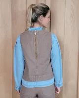 Chaleco de corte recto y largo a la cintura, confeccionado en denim con estampado de rayas verticales en tonos azul y blanco. Presenta cuello redondo y costuras visibles que definen su estructura.