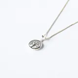 Conjunto de collar y aros con dije circular que presenta un diseño de árbol de la vida calado sobre una base de nácar, elaborado en plata.