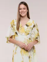 Vestido midi de gasa liviana con estampado floral en tonos amarillo y blanco, escote en V cruzado, mangas cortas amplias tipo capa, cintura entallada y falda con vuelo y ruedo irregular.