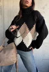 Polerón de tejido grueso con cuello alto, diseño de rombos en tonos negro, beige y blanco, y mangas largas con puños ajustados.