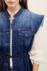 Chaleco de denim azul de corte estructurado y sin mangas, con cuello mao y cierre frontal con botones. Presenta bolsillos frontales con solapa y detalles deshilachados en las sisas y el ruedo.