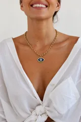 Collar de cadena de eslabones rolo en acero dorado, con dije colgante esmaltado en forma de ojo turco en tonos azul, blanco y negro con detalles brillantes.