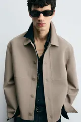 Sobrecamisa color beige de corte cuadrado, con cuello solapa, manga larga con puños abotonados, bolsillos laterales y cierre frontal con botones.