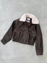 Campera estilo aviador de cuero desgastado en tono marrón oscuro, con cuello de corderito sintético desmontable en color crema. Presenta cierre frontal, bolsillos con solapa y cintura elástica.