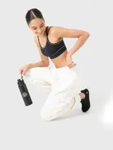 Top deportivo negro con detalle de vivo blanco en el escote, tirantes finos ajustables que se cruzan en la espalda y fruncido central en el pecho. Incluye almohadillas removibles.